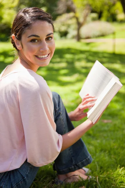Mulher olha para o seu lado enquanto lê um livro em um parque — Fotografia de Stock