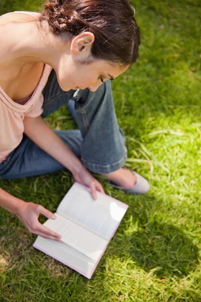 Жінка дивиться вниз на книгу, сидячи на траві — стокове фото