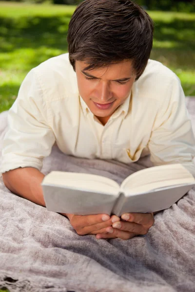 Człowiek, czytanie książki, podczas gdy on leży na kocu — Zdjęcie stockowe