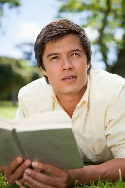 El hombre mira a la distancia mientras lee un libro mientras miente. —  Fotos de Stock