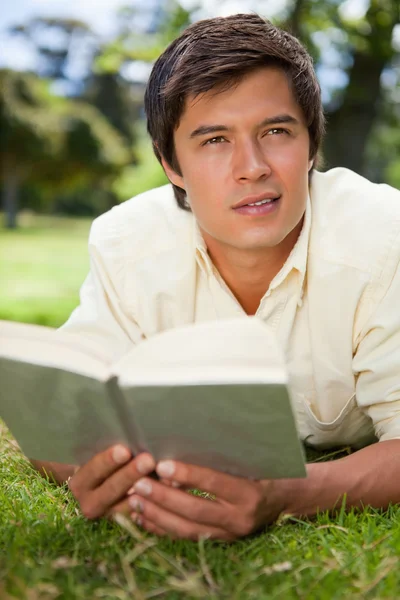 Mann schaut beim Lesen eines Buches in die Ferne, während er auf Gras liegt — Stockfoto