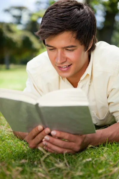Człowiek uśmiechający się czytając książkę, jak on leży w — Zdjęcie stockowe
