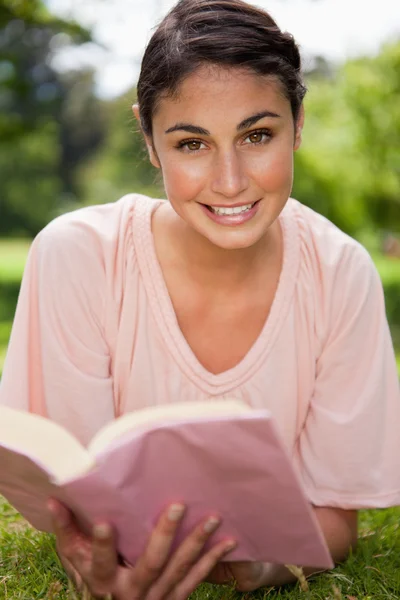 Frau blickt voraus, während sie im Liegen ein Buch liest — Stockfoto