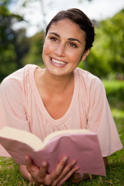 Woman looks upwards while reading a book as she is lying down — Stock Photo, Image