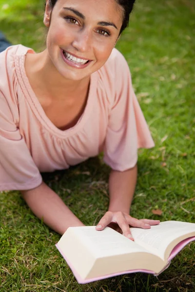 Mulher sorridente olhando para cima enquanto lê um livro enquanto ela se deita — Fotografia de Stock