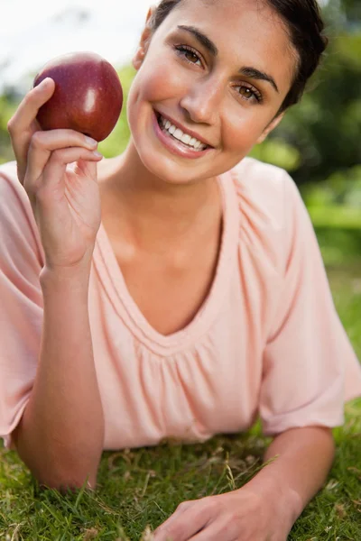 Жінка тримає яблуко, лежачи в траві — стокове фото