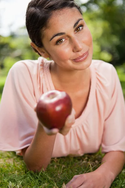 Woman offers an apple while lying in grass — Stock Photo, Image