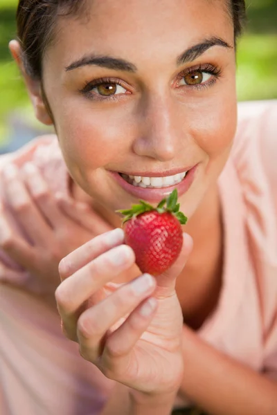 Frau bietet im Gras liegend eine Erdbeere an — Stockfoto