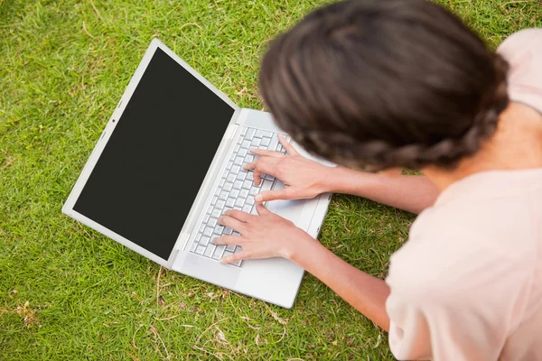 Mulher usando um laptop enquanto deitado na grama — Fotografia de Stock