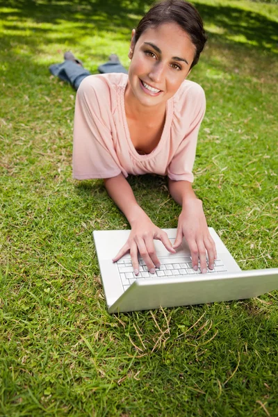 Жінка дивиться вперед, використовуючи ноутбук, коли вона лежить в сірому — стокове фото
