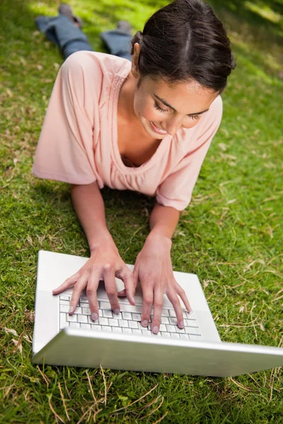 Γυναίκα χαμογελά καθώς χρησιμοποιεί ένα lap-top ξαπλώνοντας — Φωτογραφία Αρχείου