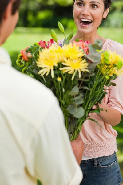 Žena překvapený jako ona je prezentována s květinami její přítel — Stock fotografie