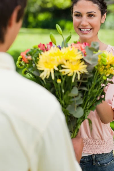Mulher sorrindo como ela é apresentada com flores por seu amigo — Fotografia de Stock