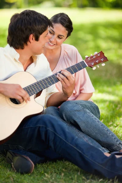 Kobieta uśmiechając się oglądając jej przyjaciel grać na gitarze — Zdjęcie stockowe