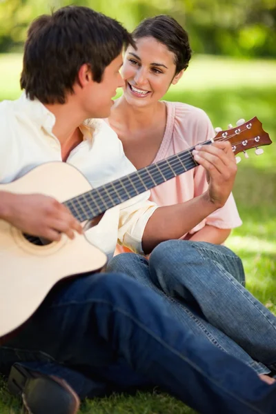 Mulher sorrindo enquanto seu amigo toca guitarra — Fotografia de Stock