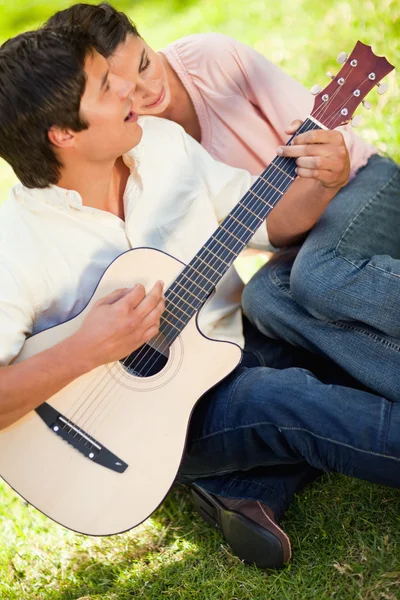 Mężczyzna gra na gitarze podczas jego przyjaciel wychyla się na jego ramieniu — Zdjęcie stockowe