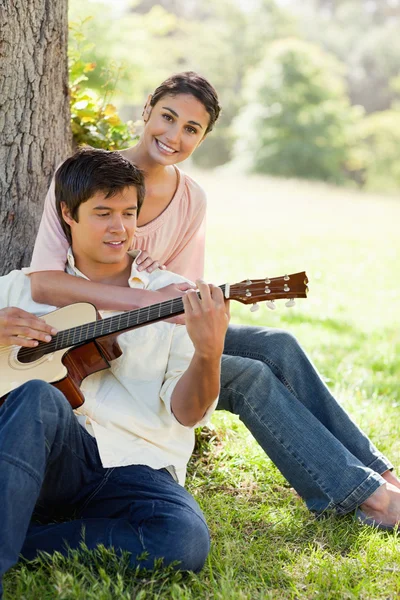 Woman holding her friend as her plays the guitar — Stock Photo, Image