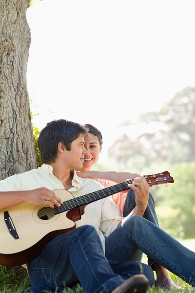Παίζοντας κιθάρα και να κάθεται σε ένα δέντρο, ενώ ο φίλος του ο άνθρωπος — Φωτογραφία Αρχείου