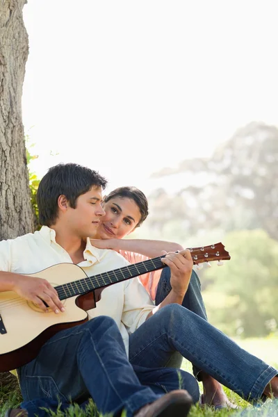 Человек смотрит вниз, играя на гитаре, а его друг смотрит — стоковое фото