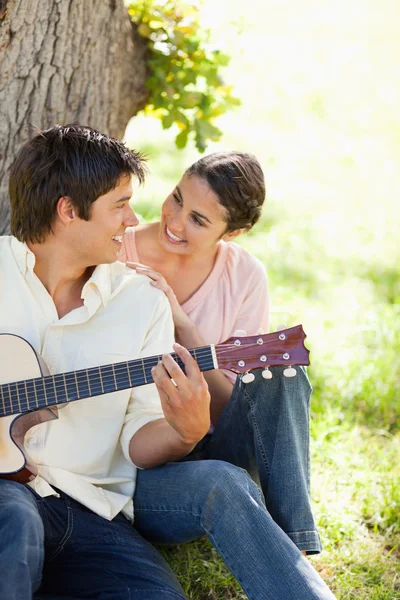 女性は、ギターを保持している彼女の友人を見ながら笑みを浮かべて — ストック写真
