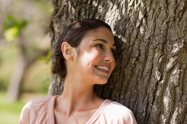 Woman looking over her shoulder while sitting against a tree — Stock Photo, Image