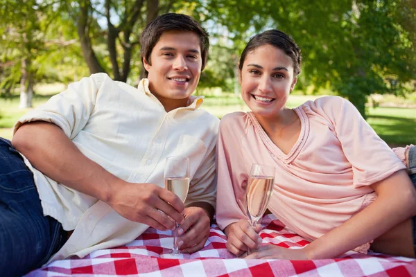 Two friends lie down on a blanket while holding champagne — Stock Photo, Image