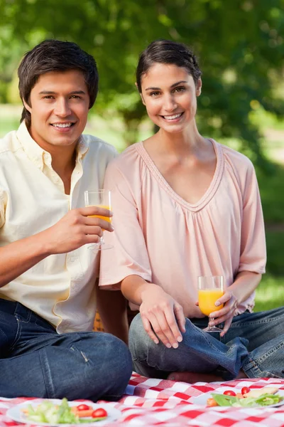 Woman and her friend smiling while holding glasses of juice duri — Stock Photo, Image