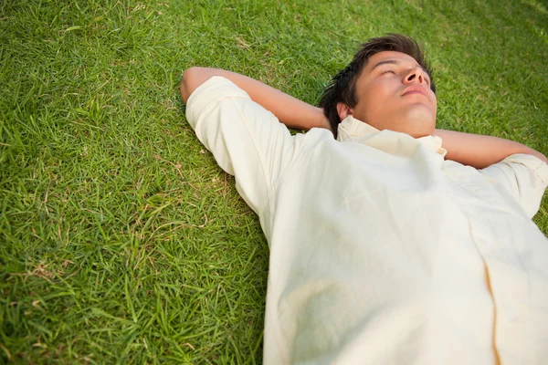 Człowiek leżący w trawie z jego oczy zamknięte i jego głowa spoczywa na — Zdjęcie stockowe