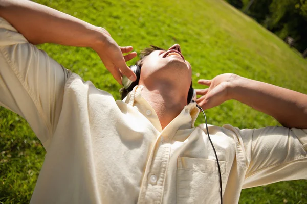 Člověk s použitím sluchátek zpívat hudbu, když ležíte v trávě — Stock fotografie