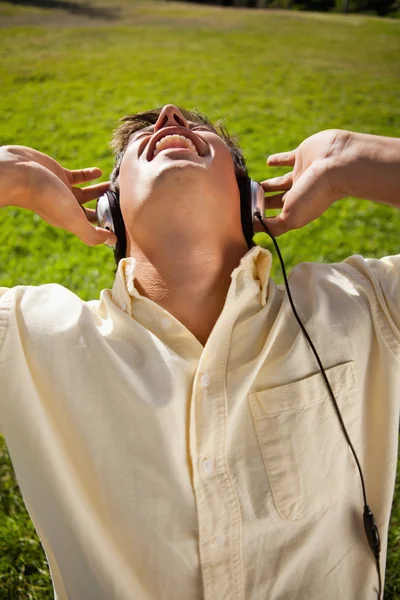 Hombre usando auriculares para cantar junto a la música mientras está sentado en gra — Foto de Stock