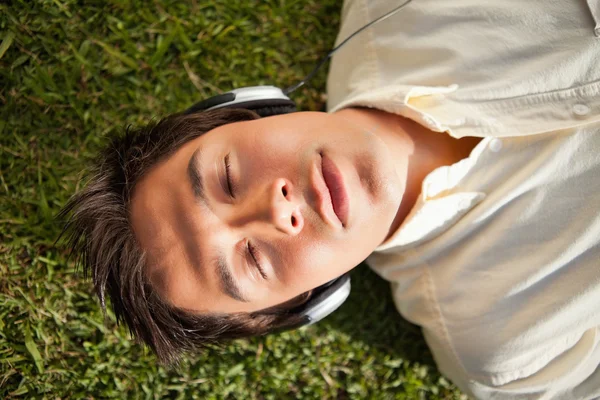 Man closes his eyes while using headphones to listen to music as — Stock Photo, Image