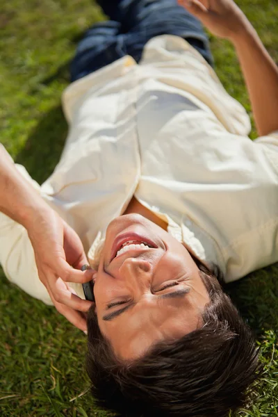 Close-up člověka smát při používání telefonu, když leží na — Stock fotografie