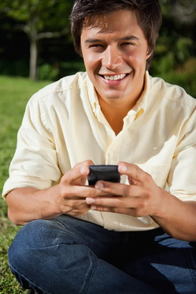 Человек улыбается, когда пишет текстовое сообщение, когда садится — стоковое фото