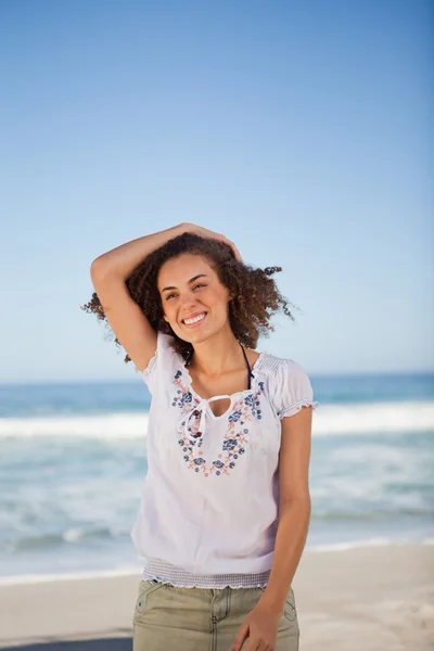 Jeune femme souriante tenant ses cheveux sur la plage — Photo