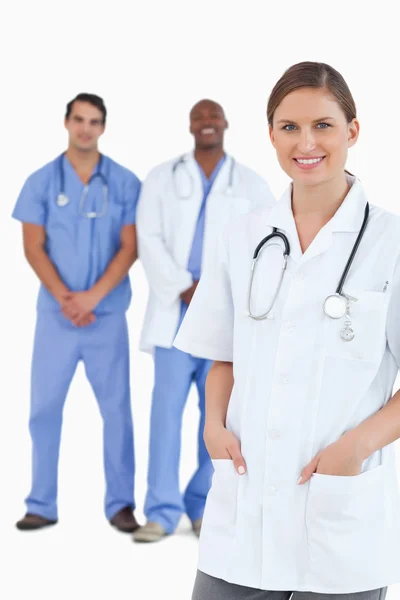 Leende kvinna läkare med manliga kollegor bakom henne — Stockfoto