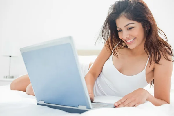 Woman lying across her bed, using her laptop and enjoying what s — Stock Photo, Image
