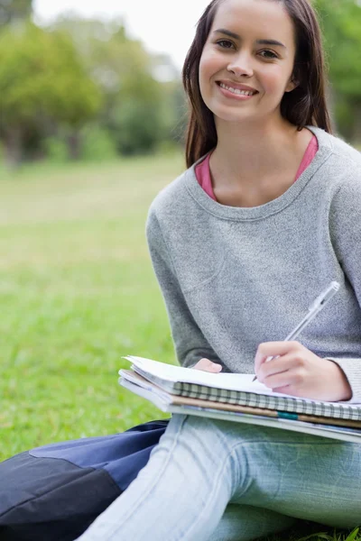 Studente sorridente che fa i compiti mentre è seduta sull'erba Foto Stock