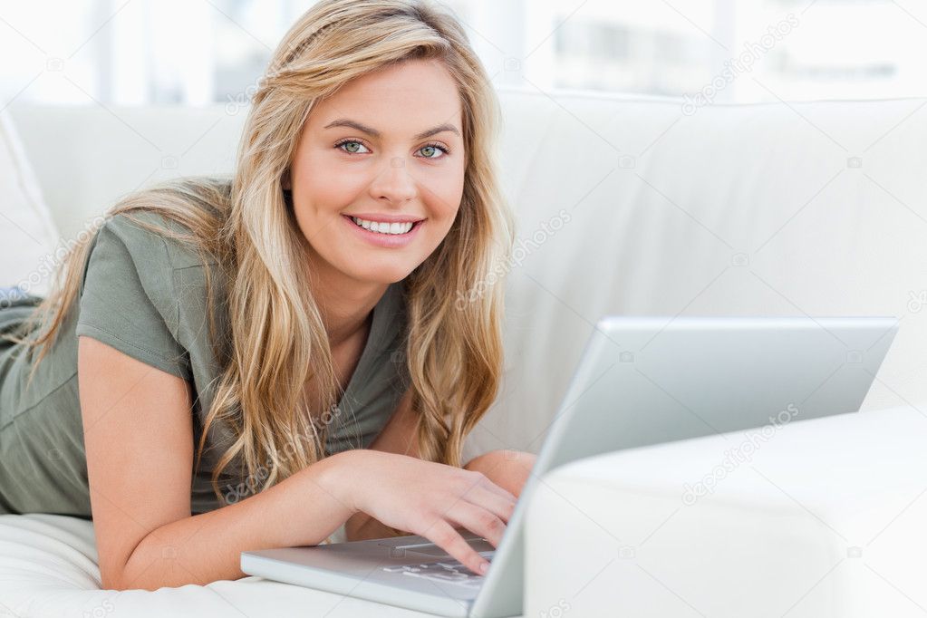 Woman lying across the couch, smiling as she looks forward, usin Stock ...