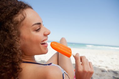 Young smiling woman holding a popsicle in front of the sea clipart