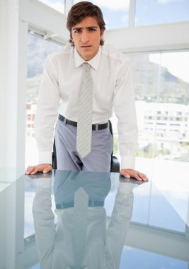 Young serious businessman leaning on a table clipart