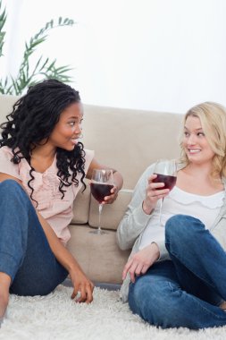 Two women sitting up against a couch are drinking wine clipart