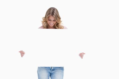 A blonde woman is looking down at a white placard she is holding clipart