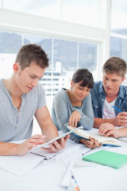 A group of students sit together using a tablet and a book to st clipart