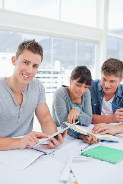 Two students use a book while the student using a tablet looks a clipart