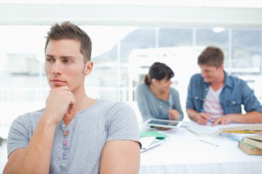 One student standing and thinking as his friends work behind him clipart