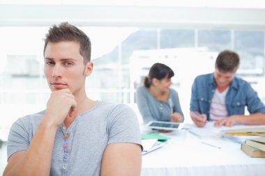 A thinking student looking into the camera with his friends behi clipart