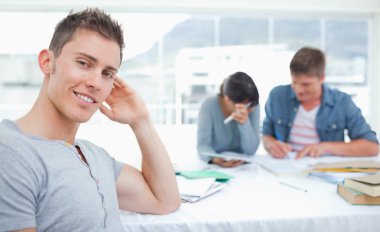 A smirking student sits in front of his friends as he looks into clipart