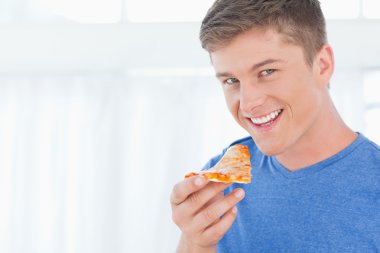 A man with a piece of pizza as he looks at the camera clipart