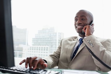 Businessman on the phone while using a computer clipart