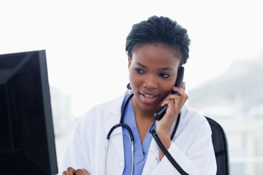 Female doctor on the phone while using a computer clipart